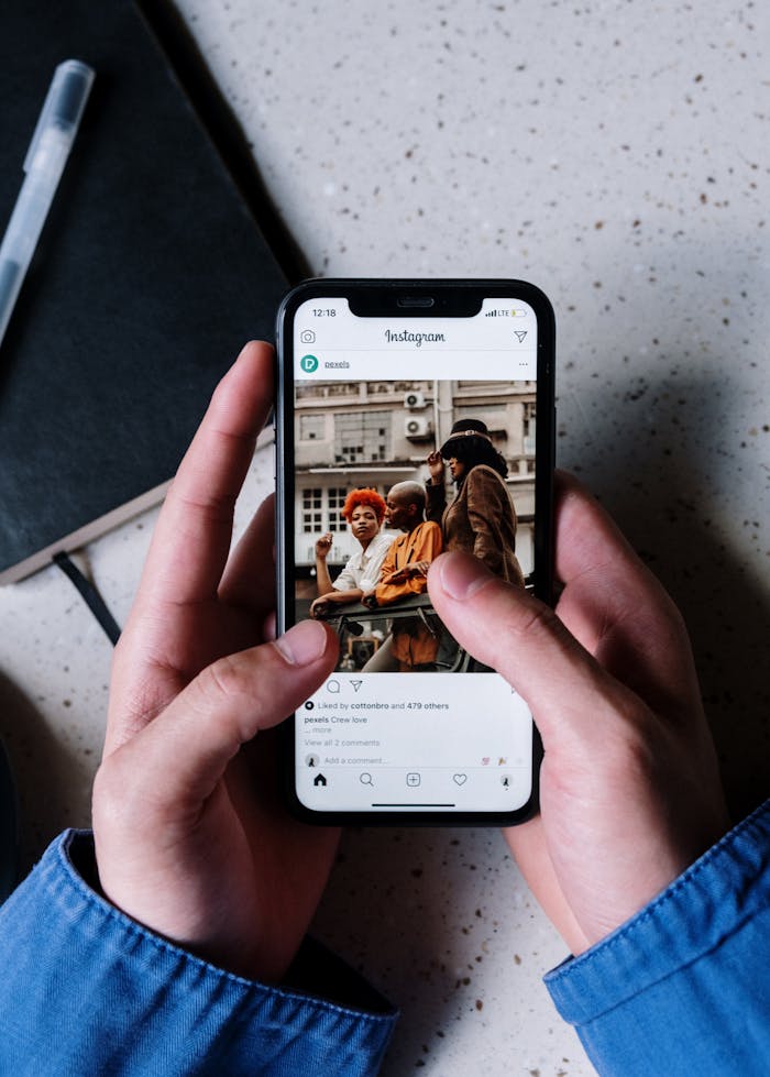 Close-up of hands holding a smartphone browsing Instagram with a notebook and pen nearby.